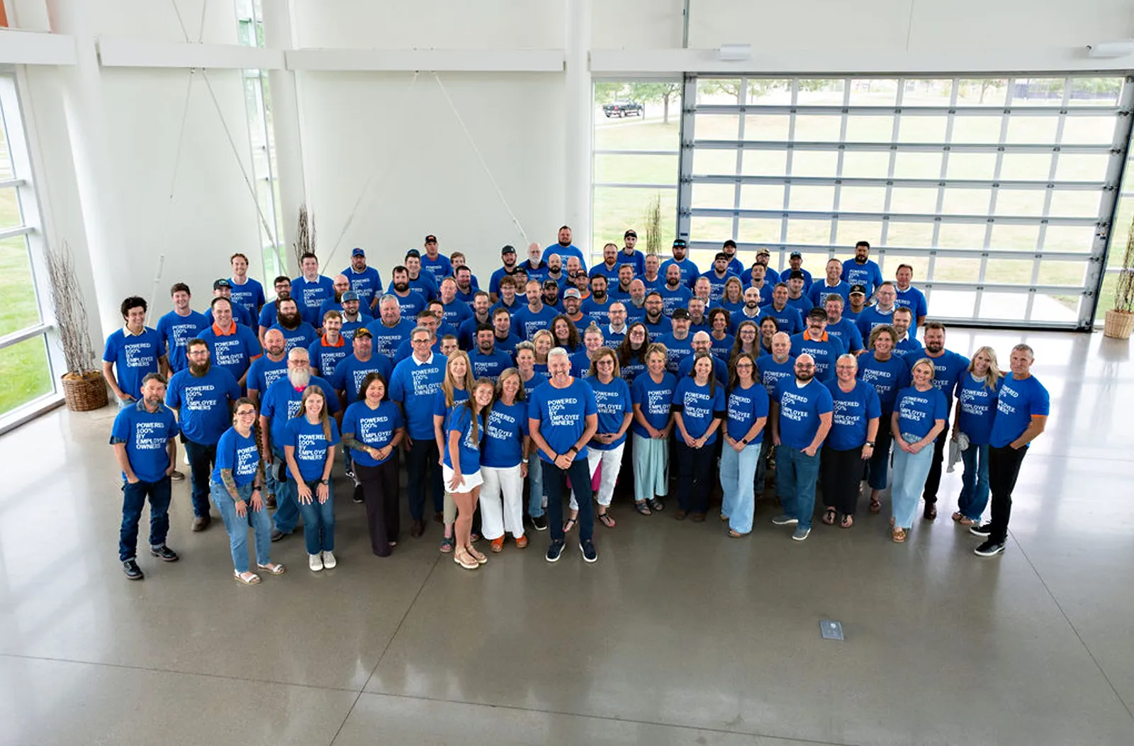 A large group of people in blue shirts standing in a large room and smiling at the camera