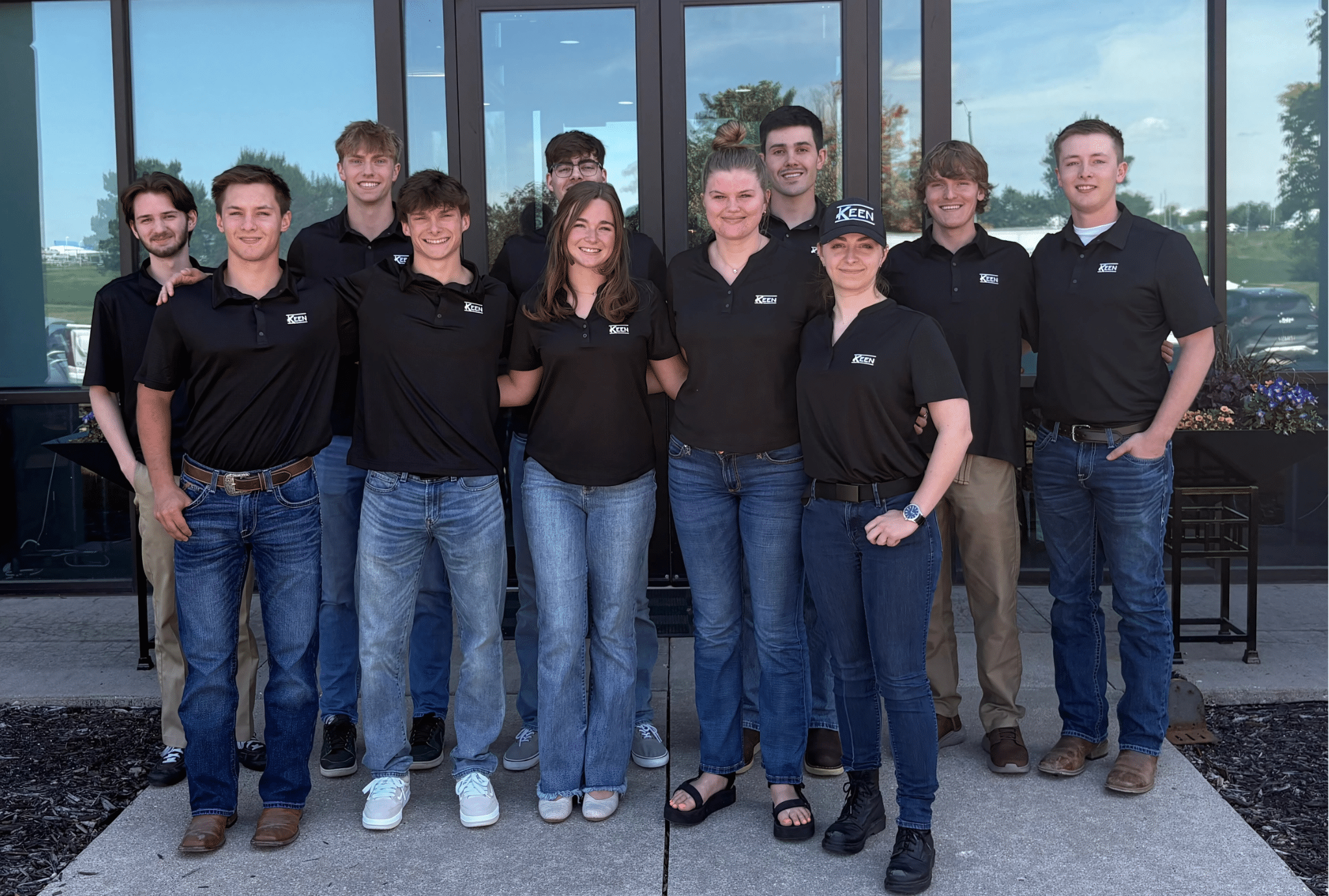 A group of Summer interns in black shirts smiling for the camera