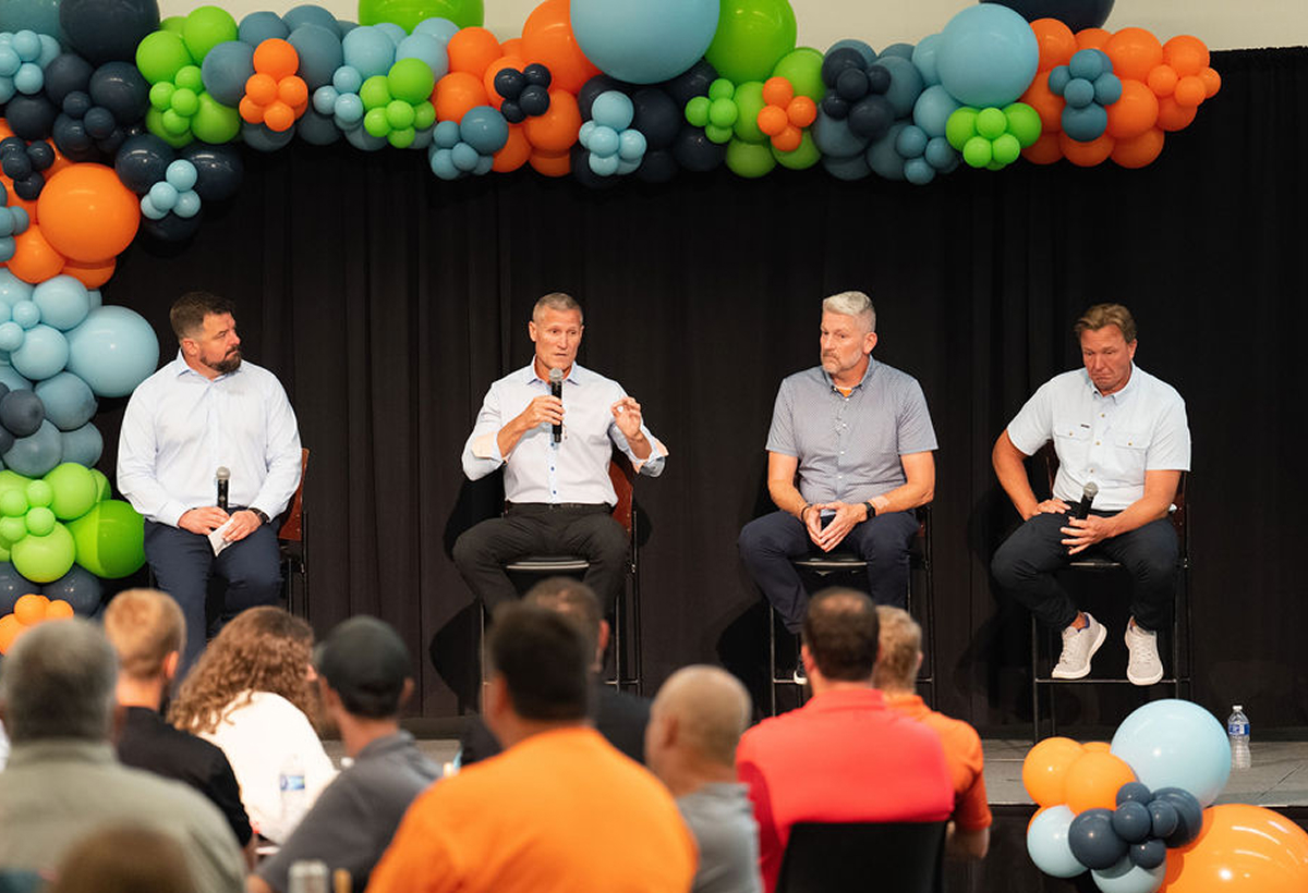 Four men sitting on chairs on stage, appearing to be hosting a Q&A panel