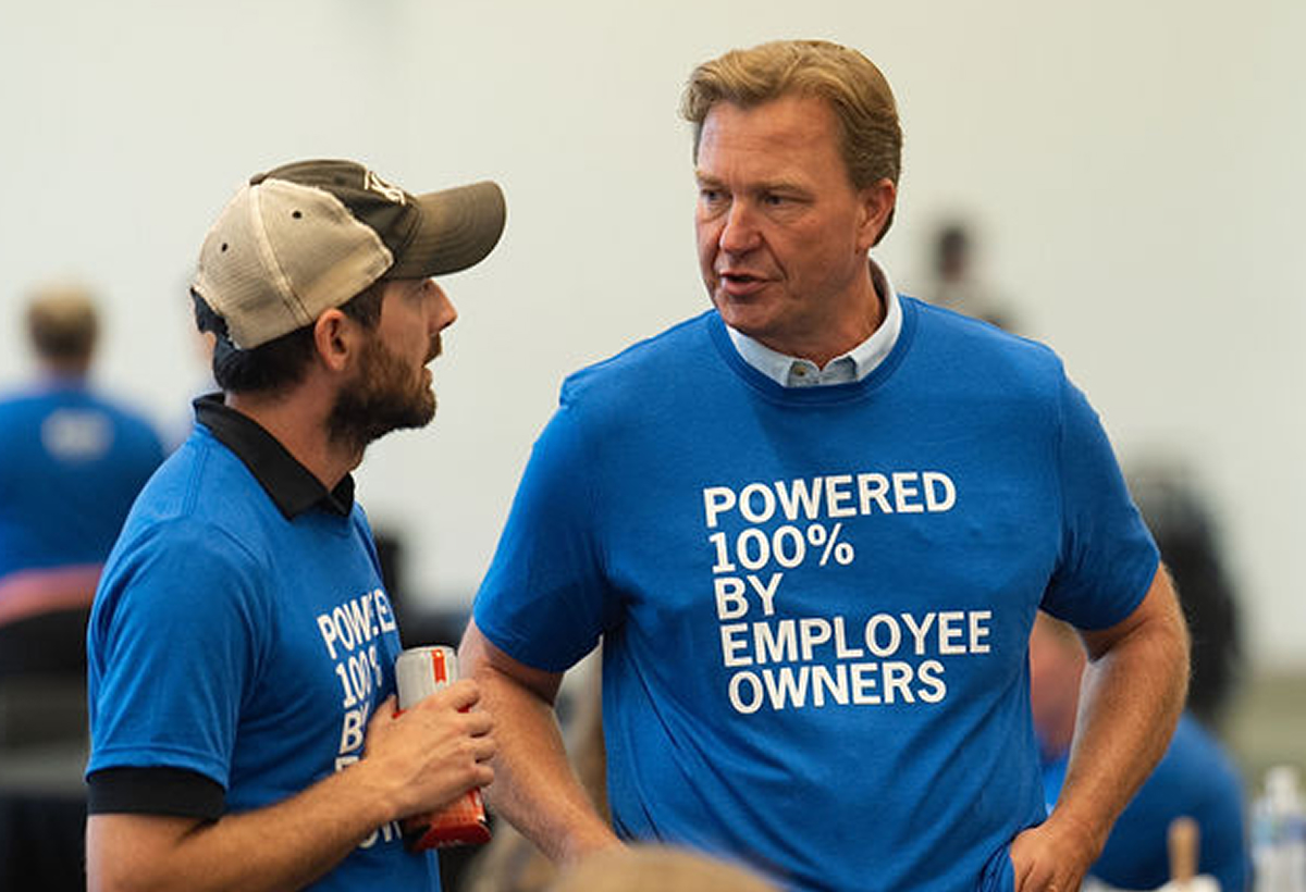 Two men having a conversation, wearing blue t-shirts reading Powered 100% by Employee Owners